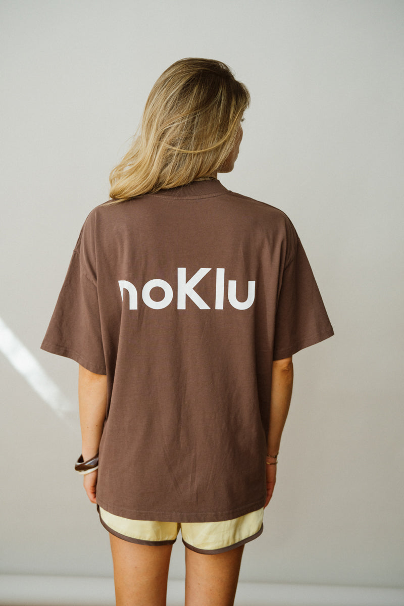 Person wearing a brown shirt with 'noKlu' logo on the back against a plain background