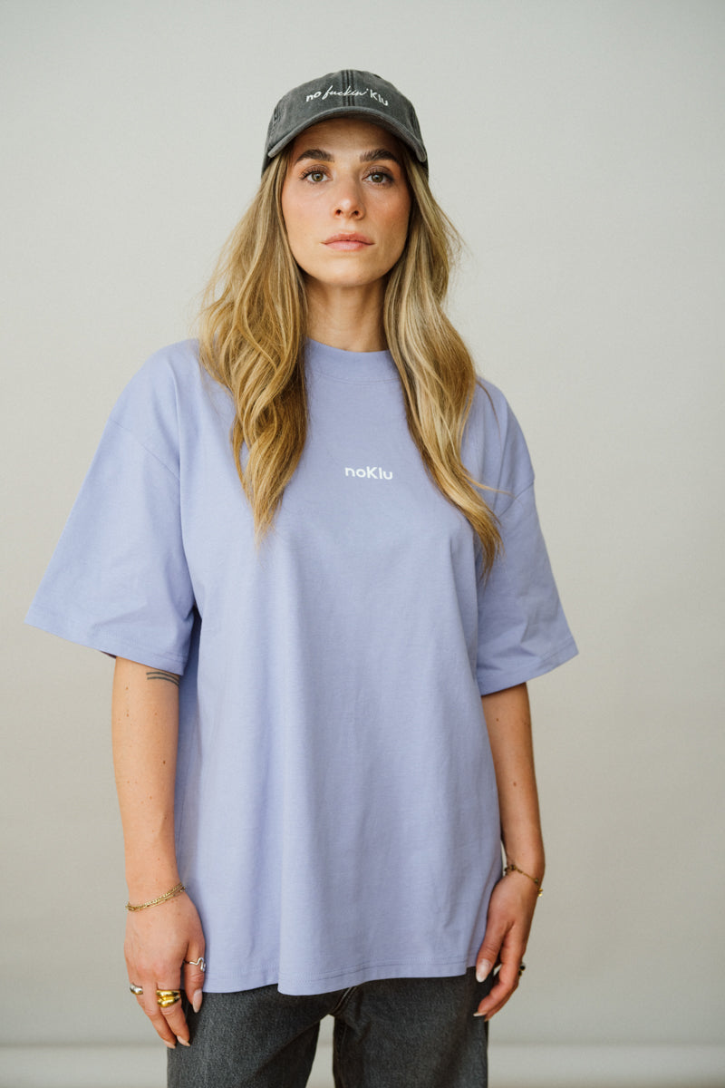 Person wearing a Lila t-shirt and dark cap against a plain background