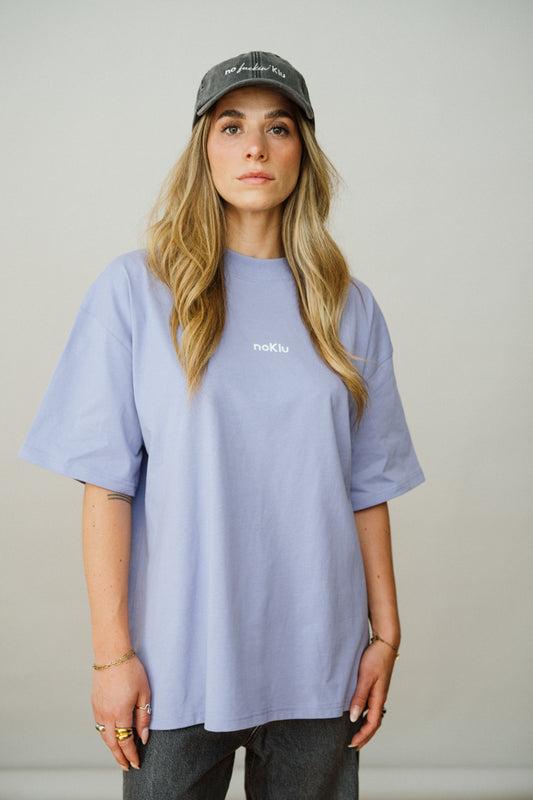Person wearing a Lila t-shirt and dark cap against a plain background