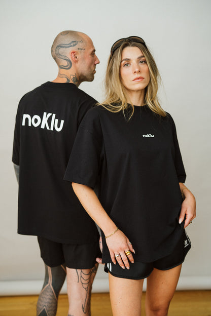 Two people wearing black t-shirts with 'noKlu' branding against a plain background