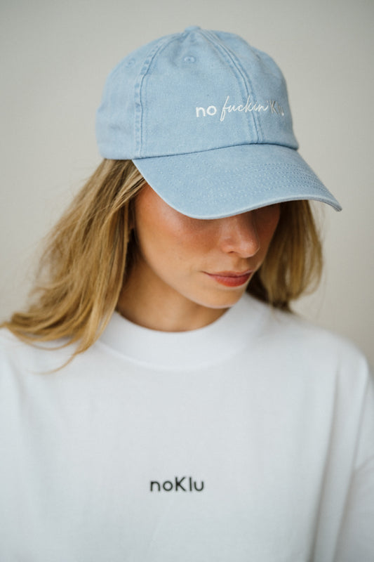 Person wearing a light blue cap with text and a white shirt with 'noKlu' branding.