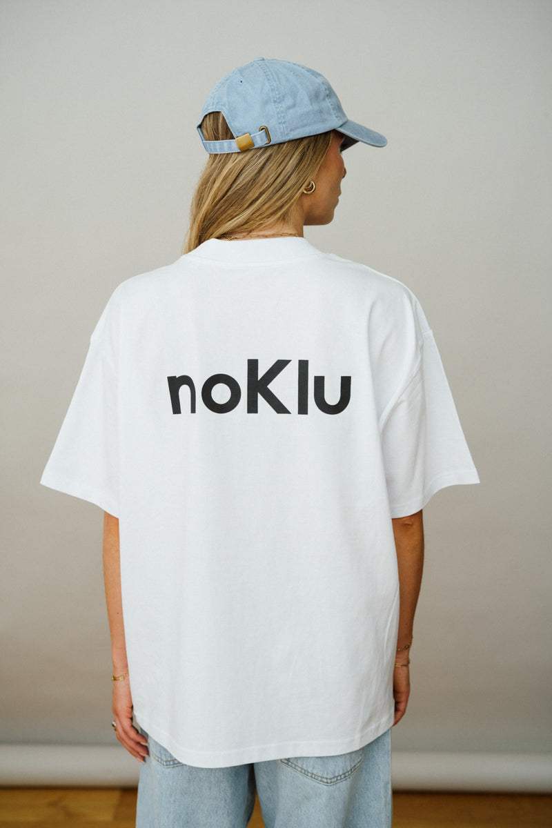 Person wearing a white t-shirt with 'noKlu' logo and a blue cap indoors.