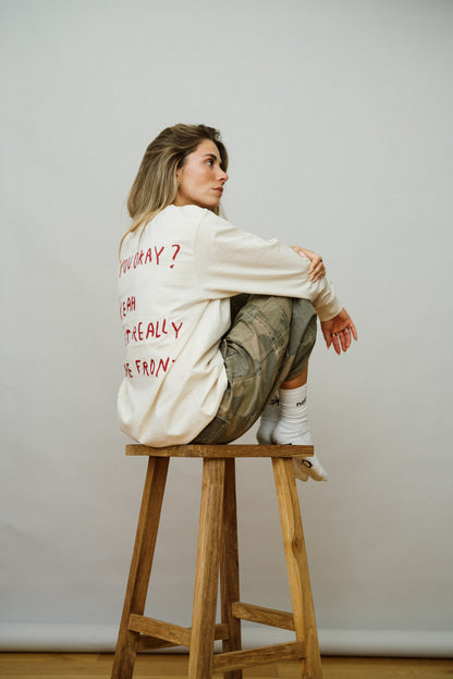 Girl sitting on stool in a light beige shirt with red text on the back

