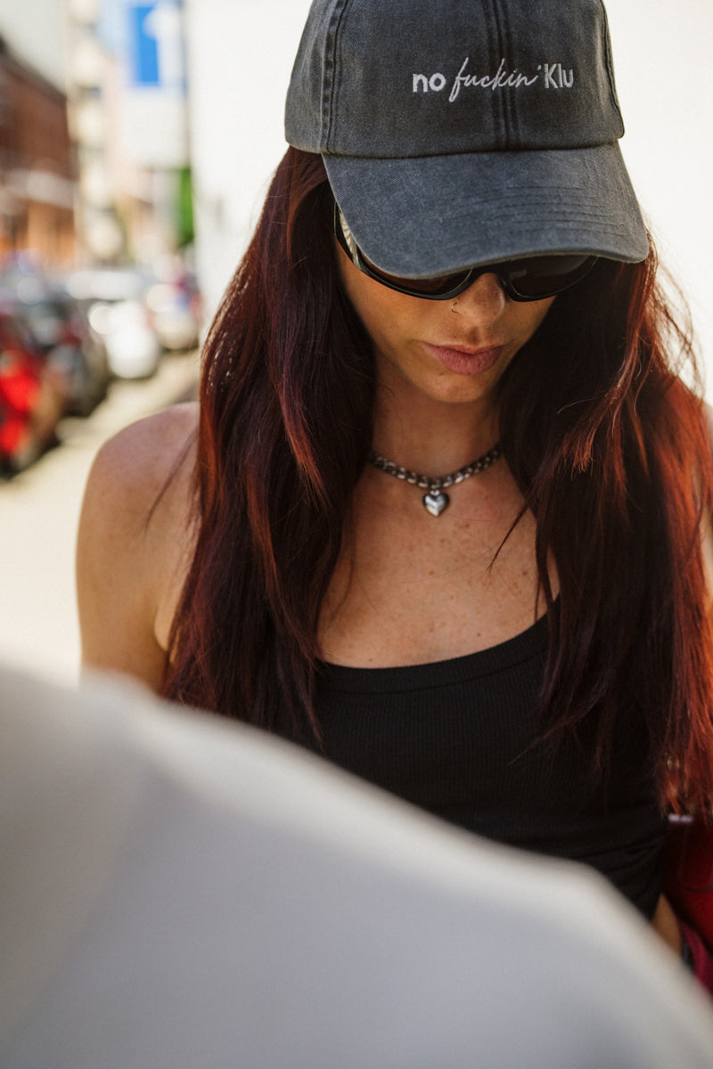 Woman wearing a cap with text on it, standing outdoors.