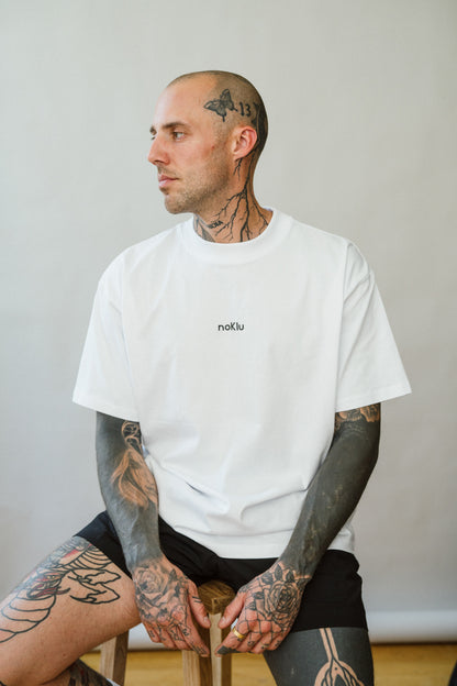 Man wearing a white t-shirt with a logo, sitting against a plain background