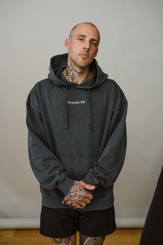 Man wearing a dark grey hoodie with visible tattoos against a plain background