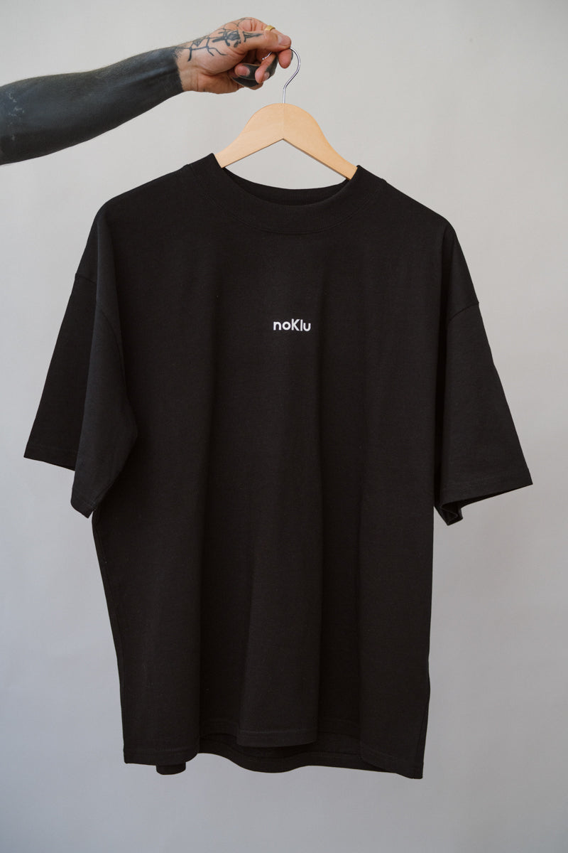 Black t-shirt with a logo on a hanger against a gray background