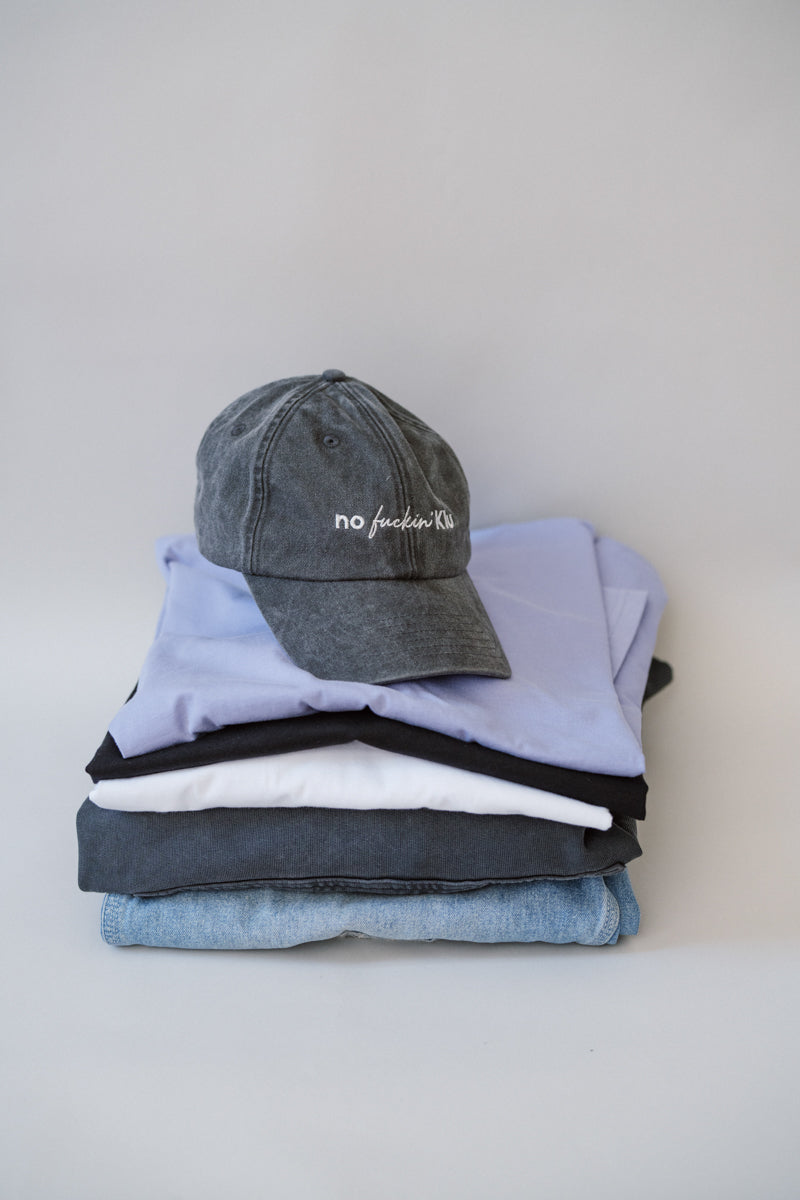 Stack of folded clothes including a cap on a light gray background